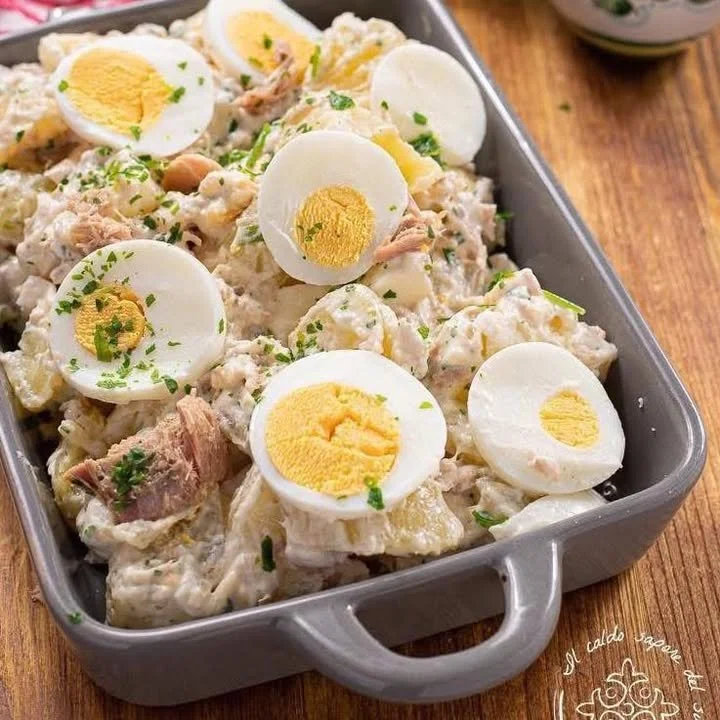 Insalata di patate tonnate servita in un piatto con decorazione di erbe fresche.