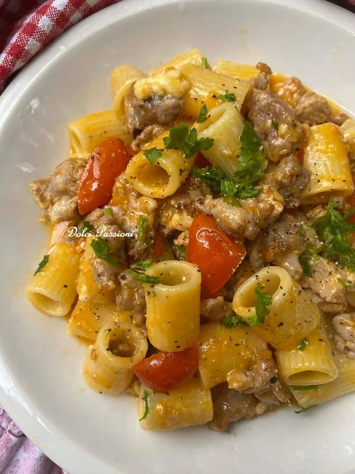 Piatto di mezze maniche con salsiccia sbriciolata e pomodorini freschi