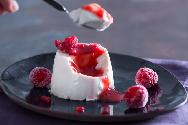 Panna cotta servita con salsa di frutti di bosco su piatto bianco.